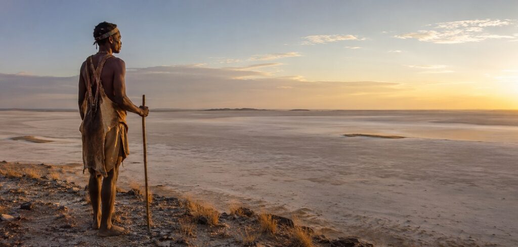 A lone traditional San tracker, stands with his tracking stick gazing over the vast Kalahari salt pan.